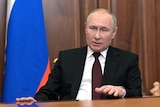 Vladimir Putin speaks in front of a Russian flag. 