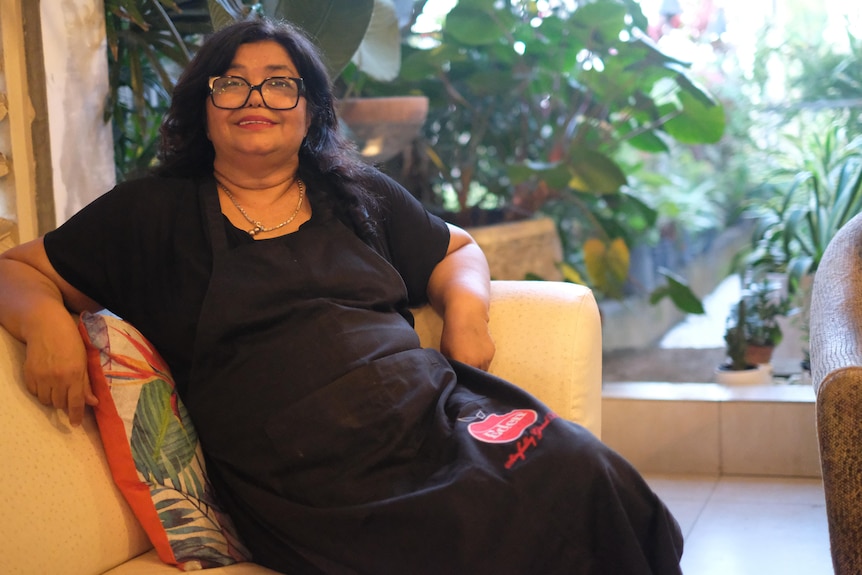 A woman sits sideways on a couch looking at the camera smiling. 