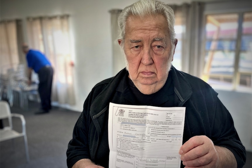 an elderly man holding up a death certificate