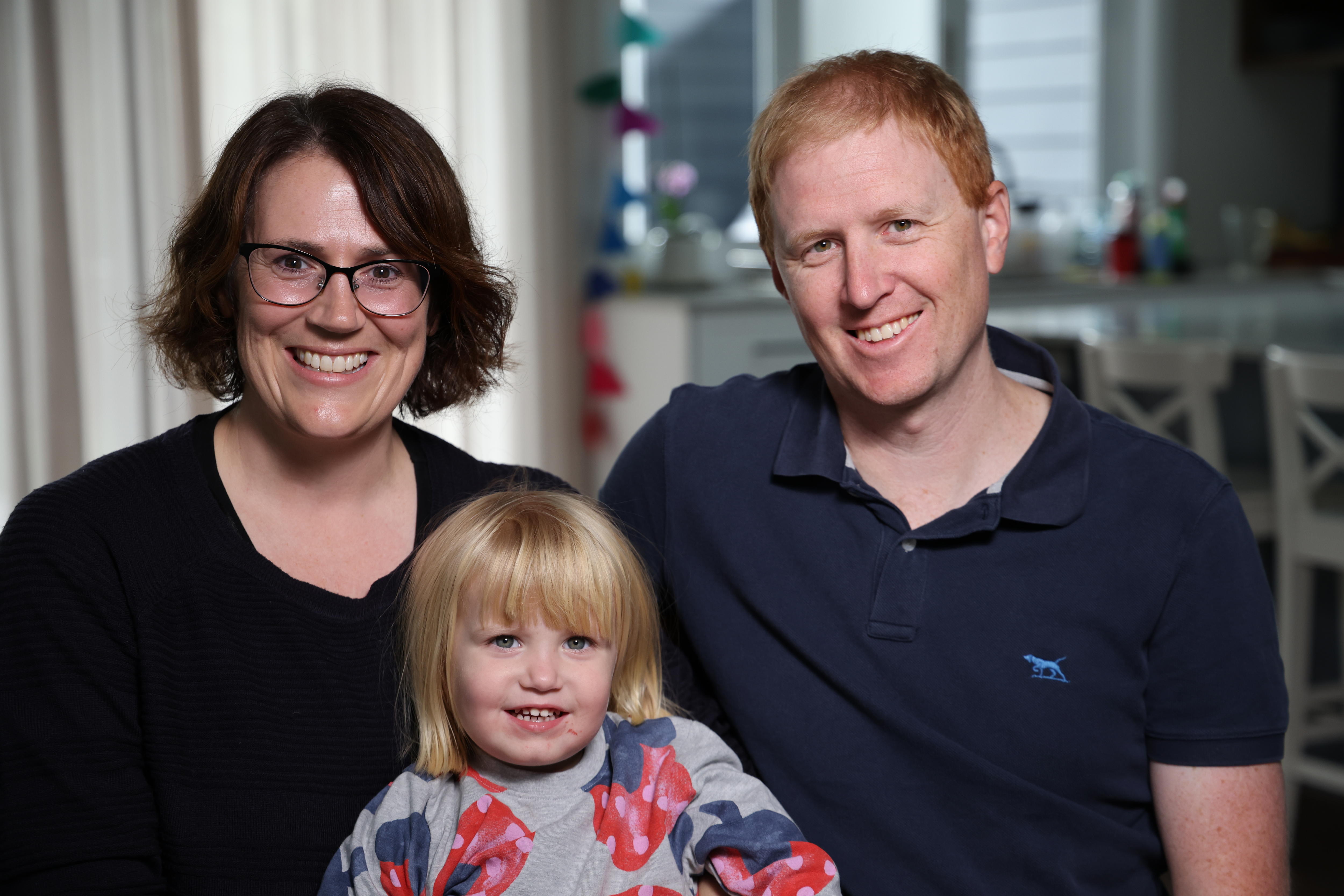 a family sitting in their loungeroom, smiling into the camera