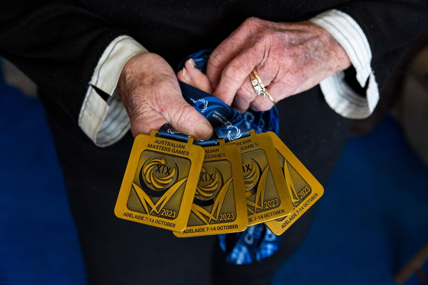 An elderly woman's hands hold four gold medals won for swimming