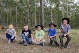 A group of students sit on a balance line among trees.