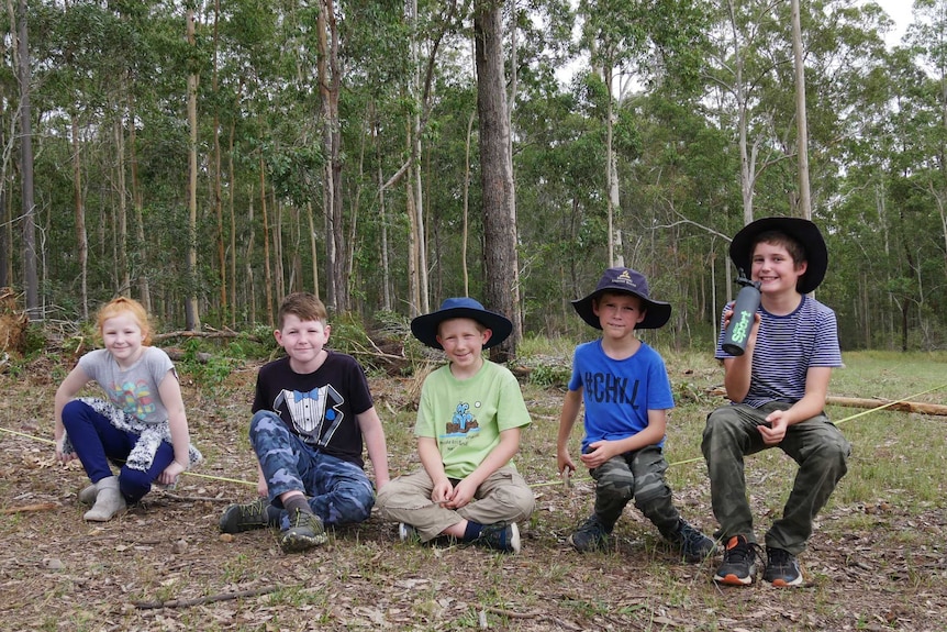 A group of students sit on a balance line among trees.