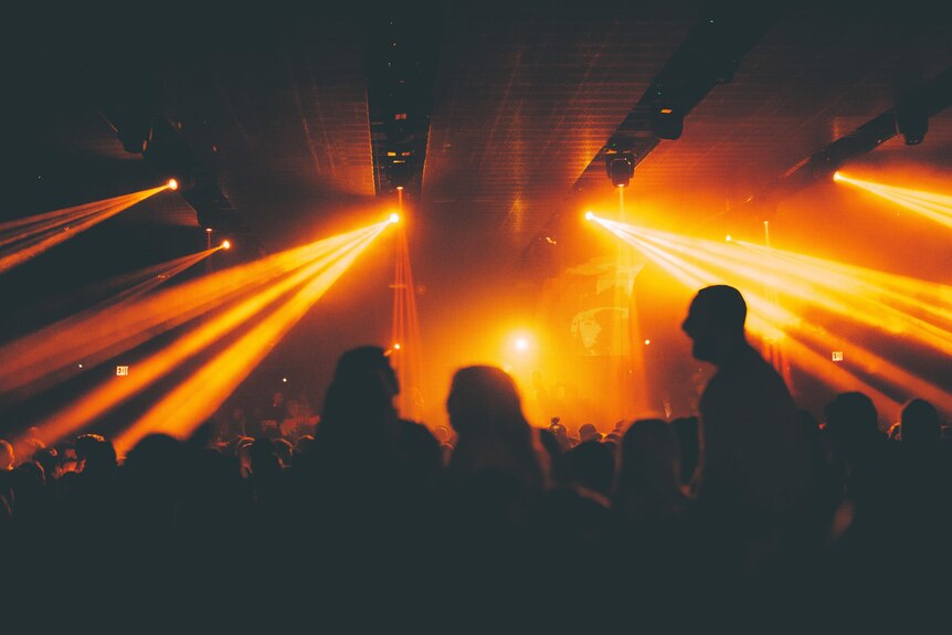 Night club scene with black silhouettes in a crowded warehouse and yellow lights