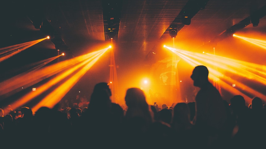 நெரிசலான கிடங்கில் கருப்பு நிழல் ஓவியங்கள் மற்றும் மஞ்சள் விளக்குகளுடன் இரவு விடுதி காட்சி.