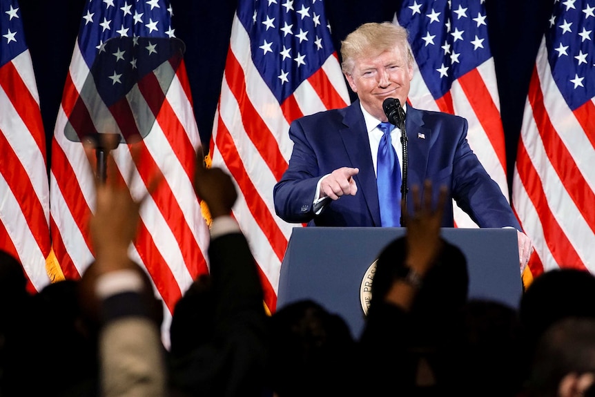 US President Donald Trump addresses a rally in front of American flags.