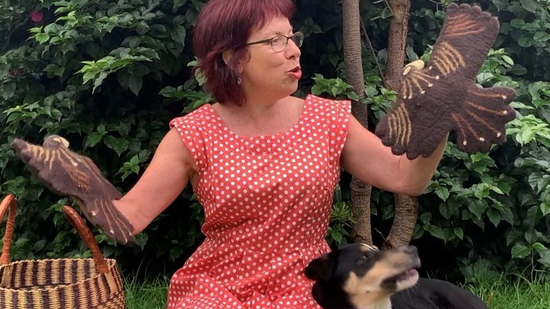 Louise holding two Bunjils (eagles) with her dog Reggie sitting on her lap