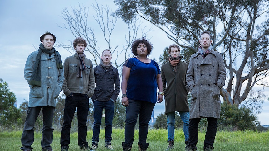 Emma Donovan and the PutBacks standing in a rural outdoor setting wearing jackets and scarves