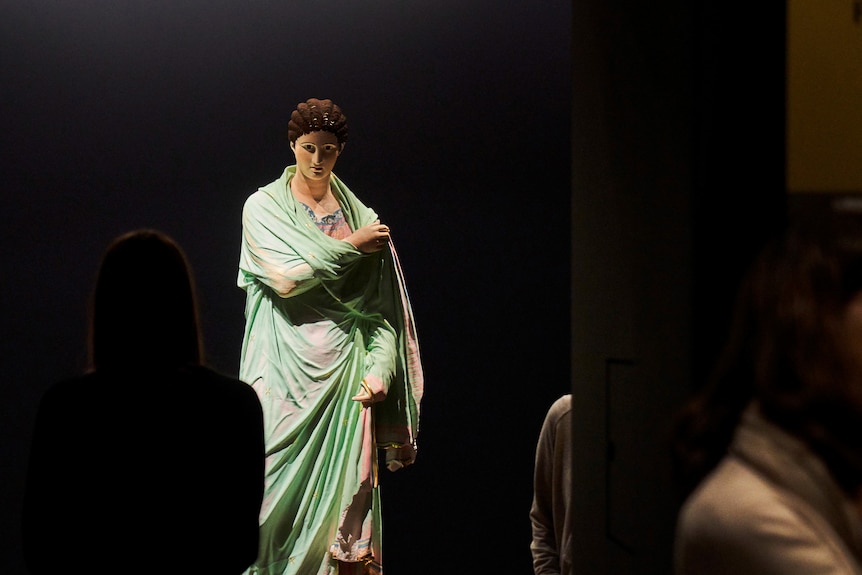 A ancient Greek sculpture of a woman clad in a flowing robe, the sculpture is painted in colour