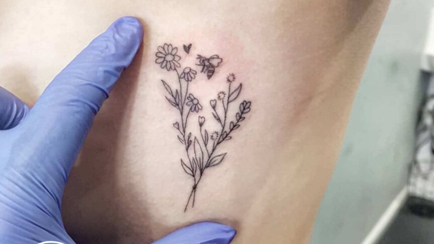 A hand in a purple glove shows how small a tattoo is of flowers and a bee.