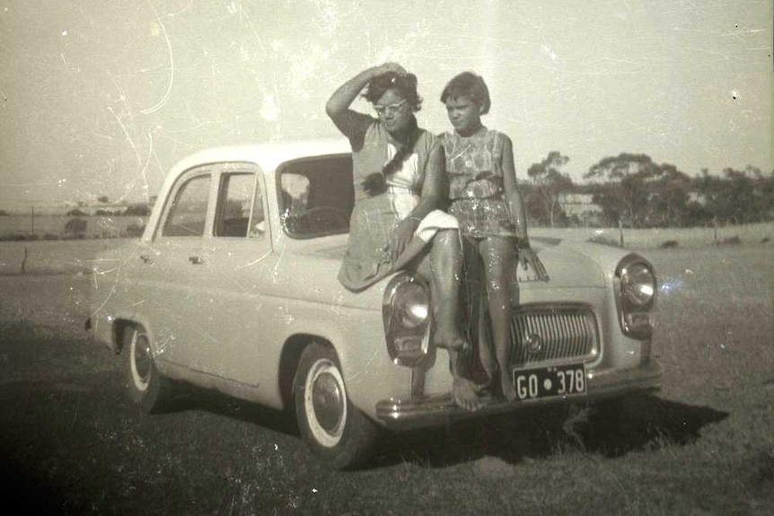 Frances and Lois Phillips on the front of a car, 1950s or 1960s.