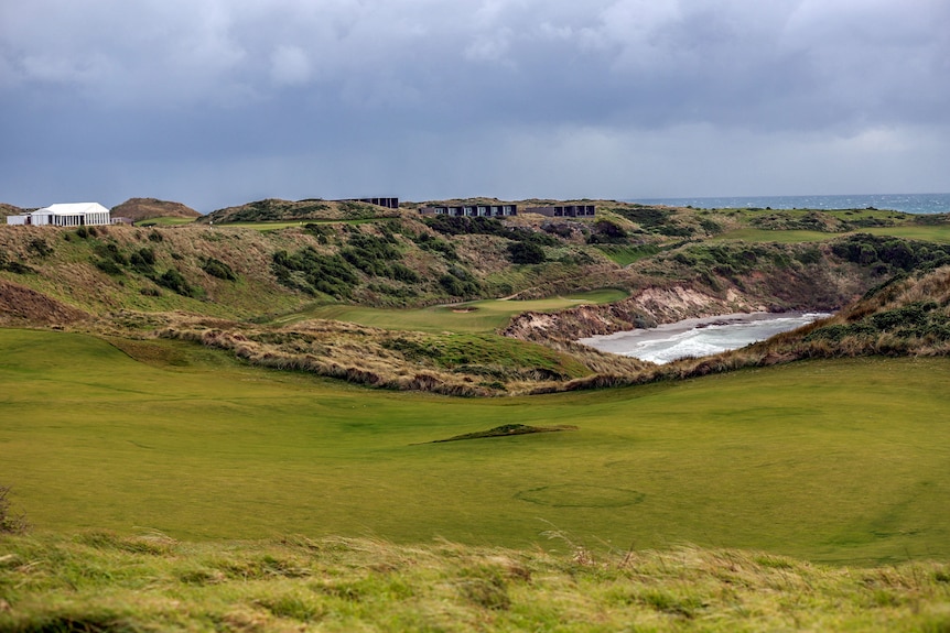 A picturesque golf course on a coast line with a row of accommodation buildings in the background 