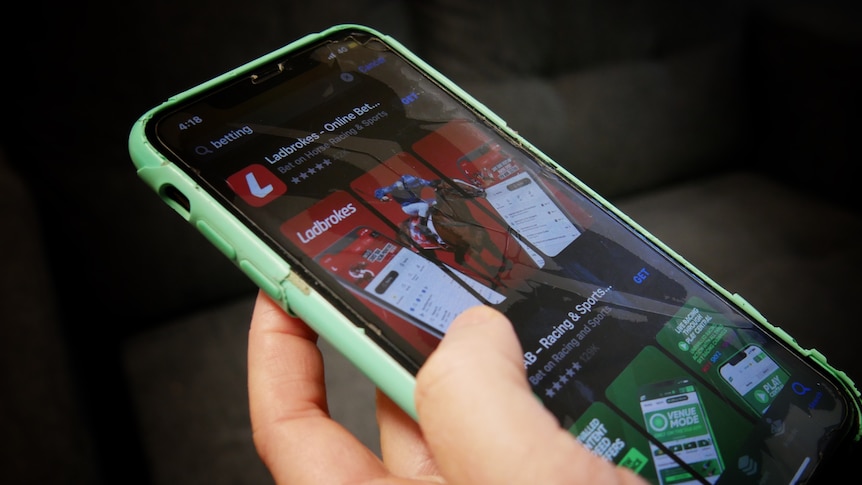 A close up on a hand holding a mobile phone with two betting company brands visible on the screen.