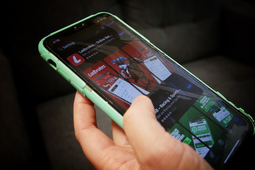 A close up on a hand holding a mobile phone with two betting company brands visible on the screen.