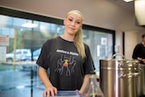 A woman in a kitchen smiles at the camera, she wears an Aboriginal justice shirt