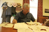 Pastoralist Simon Hilder sits at a table with old documents spread out in front of him.