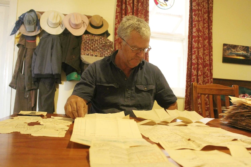 Pastoralist Simon Hilder sits at a table with old documents spread out in front of him.