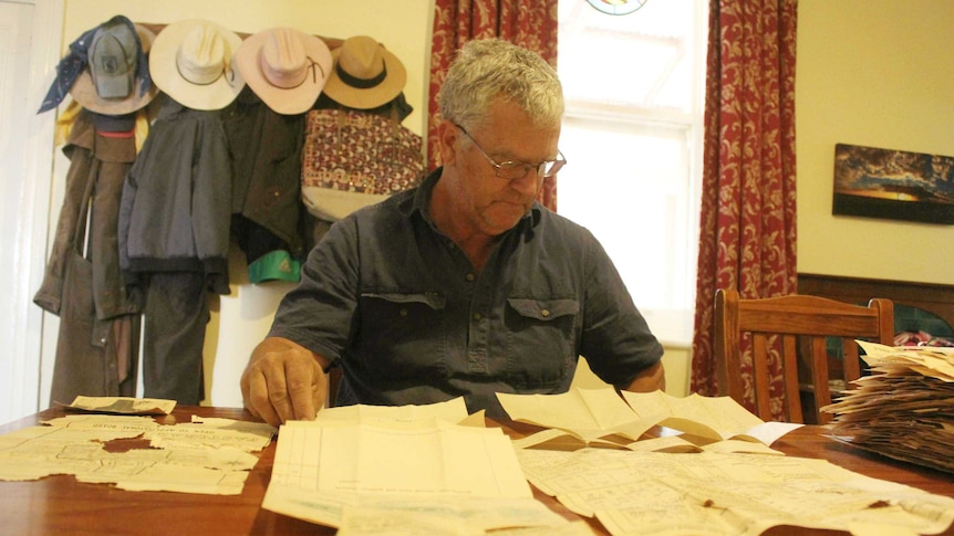 Pastoralist Simon Hilder sits at a table with old documents spread out in front of him.