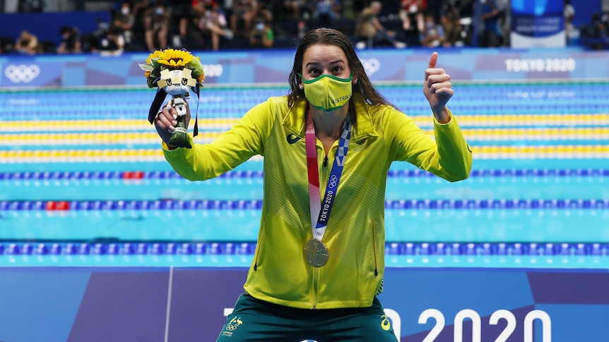 Wearing her gold medal and holding the Tokyo mascot, Kaylee McKeown gives a big thumbs up