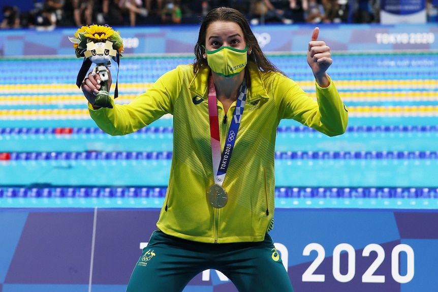 Wearing her gold medal and holding the Tokyo mascot, Kaylee McKeown gives a big thumbs up