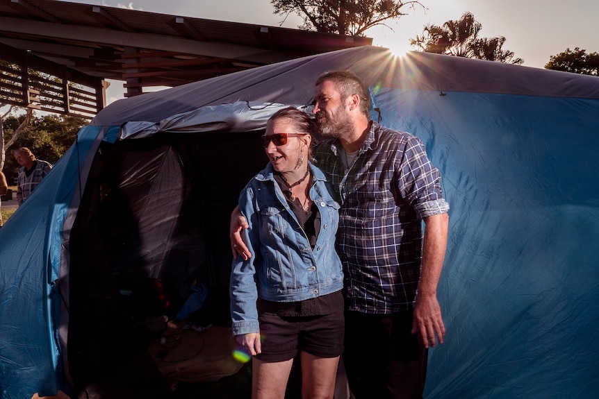 A man and woman hug outside a tent.