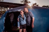 A man and woman hug outside a tent.
