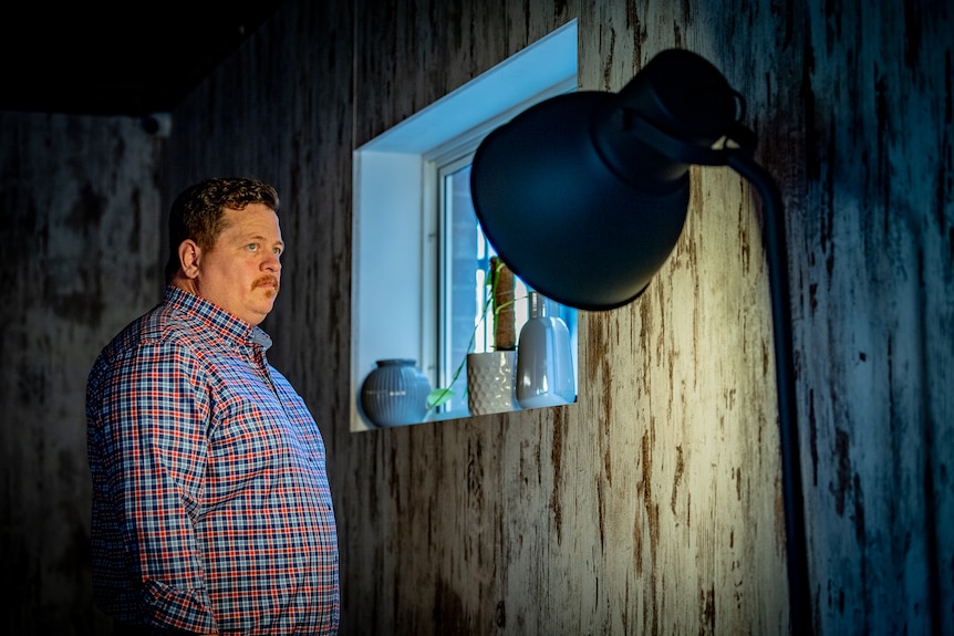 Alan Earls standing near a window and looking into the light of a lamp.