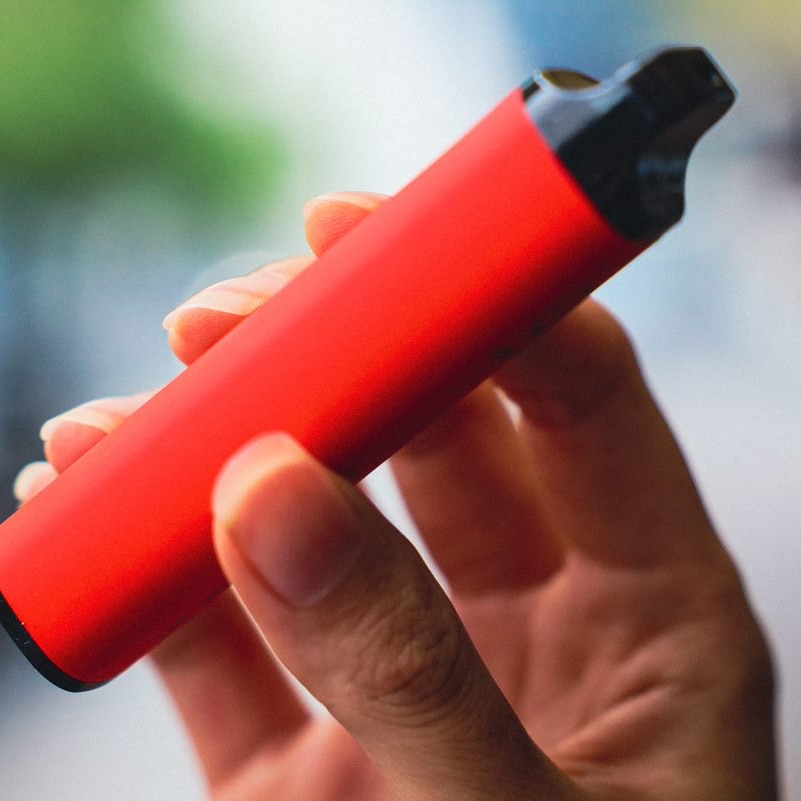 A red e-cigarette or vape held in a hand.