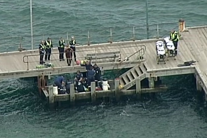 Police officers watch as paramedics work on the scuba diver on Frankston Pier.