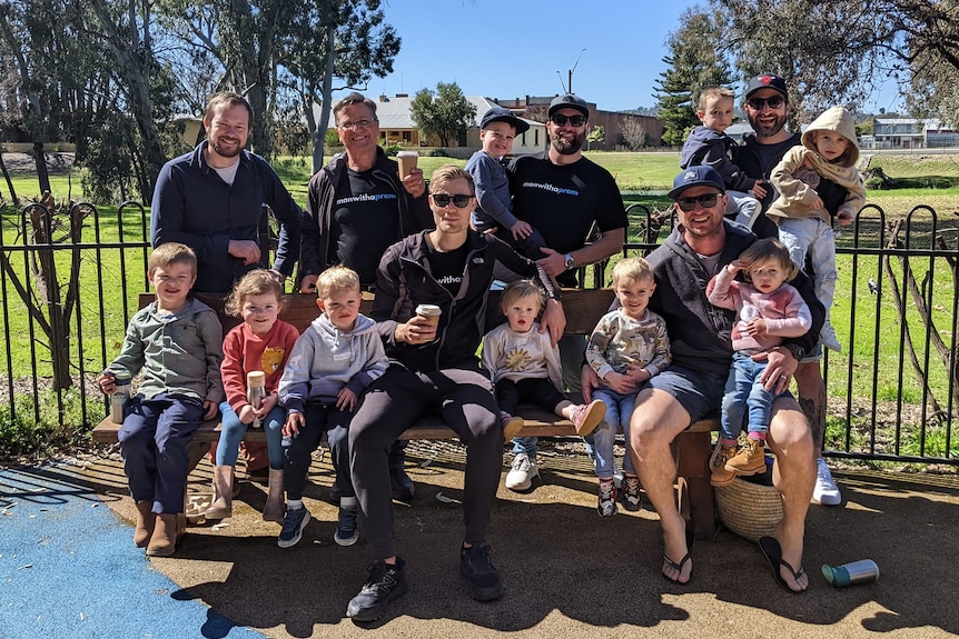 A group of regional dads sit on a park bench with their children, enjoying coffee and a chat.