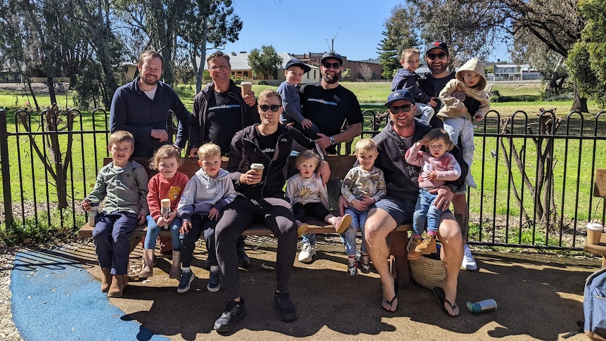 A group of regional dads sit on a park bench with their children, enjoying coffee and a chat.