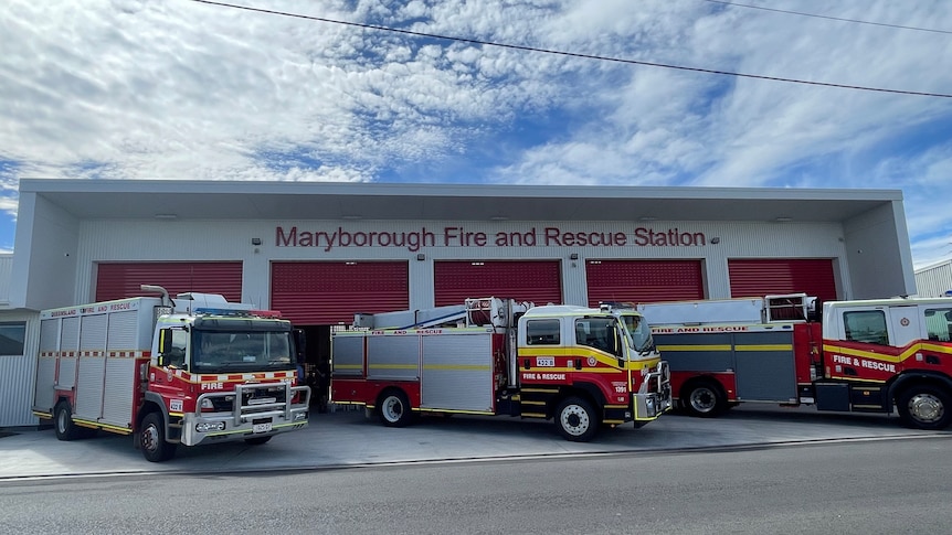 A white and red building with fire trucks in front, under a cloudy sky,  Maryborough Fire And Rescue Station written on top