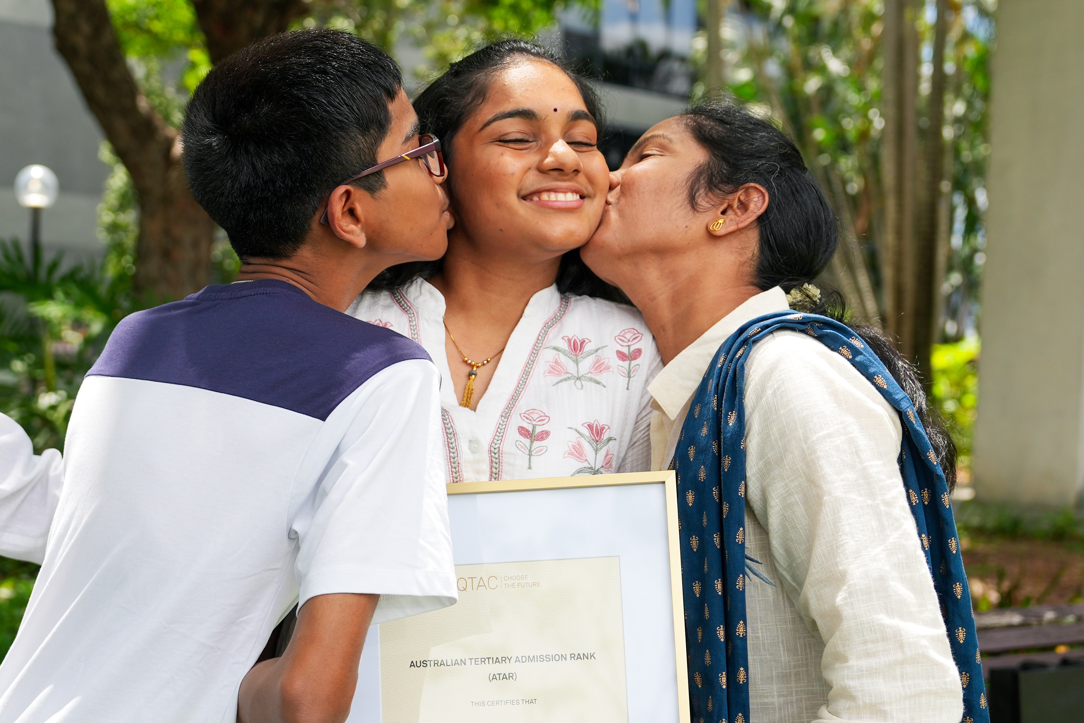 Una joven recibe un beso en la mejilla de su madre y su hermano.