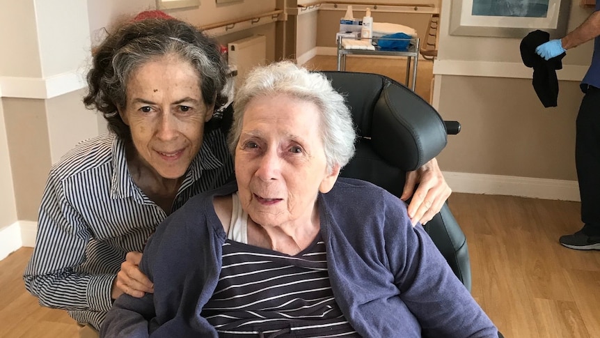 Patricia is sitting down and Therese is crouching behind her will arms around her chair.