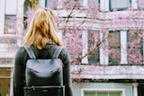 Girl standing with her back to the camera, wearing a backpack. 