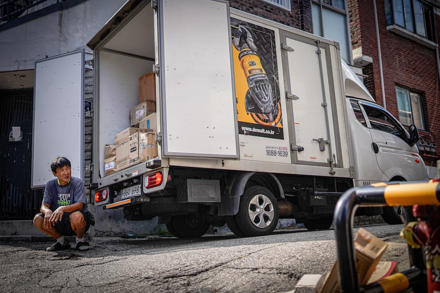 Lee Seong Wook squats behind his delivery truck.