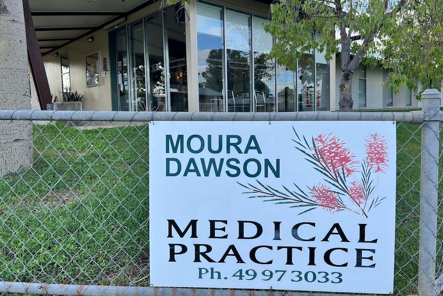 A sign on a fences reads "Moura Dawson Medical Practice" in front of a building.