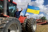 A farmer waves from a tractor that has a Ukrainian flag attached to it.
