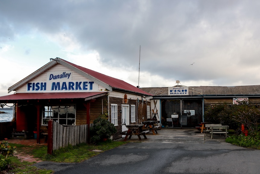 Old wooden building that reads Dunalley fish market with coastline in background