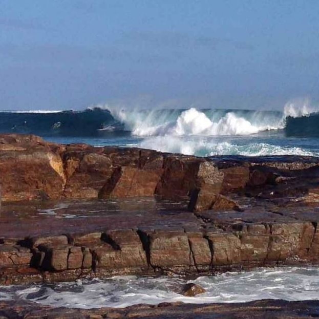 A rocky shoreline with large crashing waves in the background.