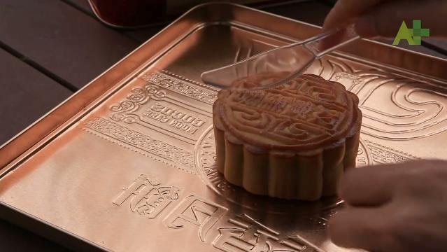 A hand holds a knife and cuts through a mooncake