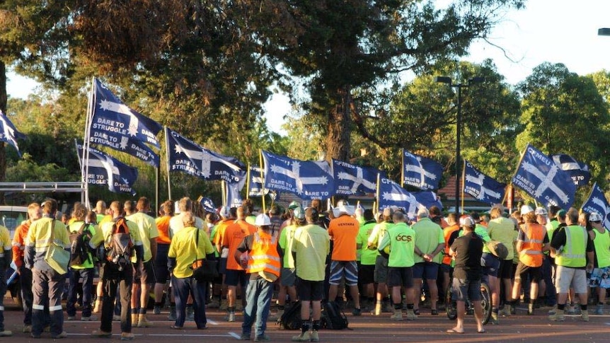 A large group of union members with their backs to the camera hold CFMEU flags at the Perth Children's Hospital site.