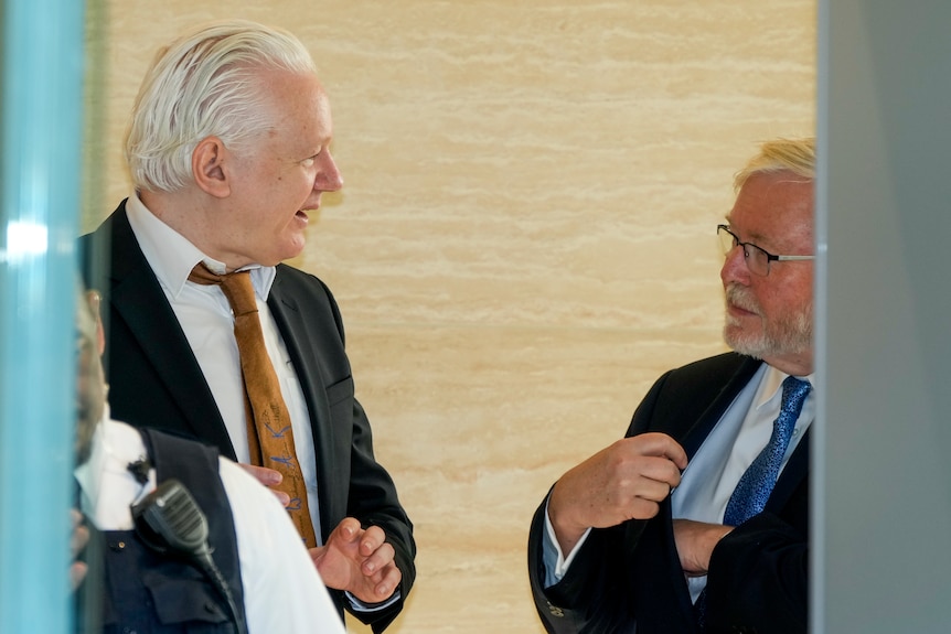 A side shot of two men wearing suits in a conversation with each other