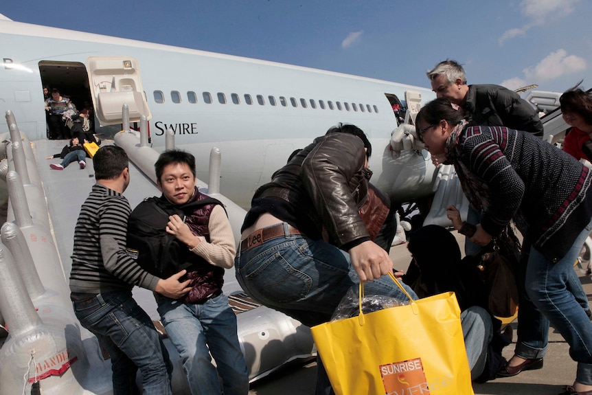 People slide down an emergency exit slide from a 747, some carrying duty free bags