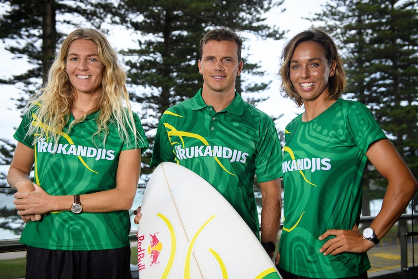 Two Australian female surfers stand alongside a male teammate at a photo shoot in Sydney.