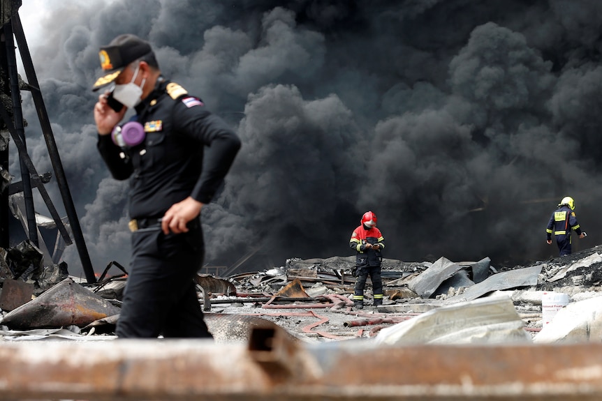 A rescue worker stands in the foreground in the phone while the entire sky behind him is covered in black smoke.