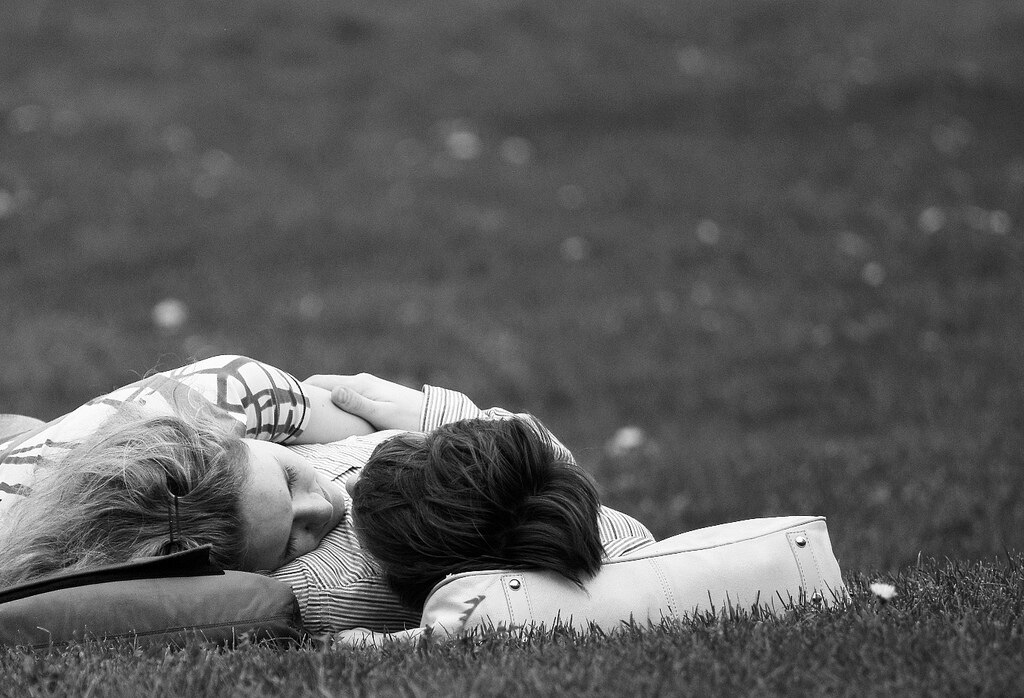 A couple lie in the grass, heads tilted towards each other.