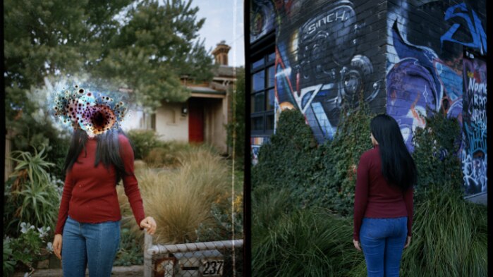 A woman standing in front of a house and graffitied wall with her face obscured