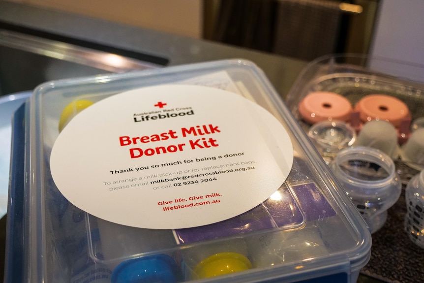 A close up of a plastic container labelled as a breast milk donor kit next to baby bottles on a kitchen bench