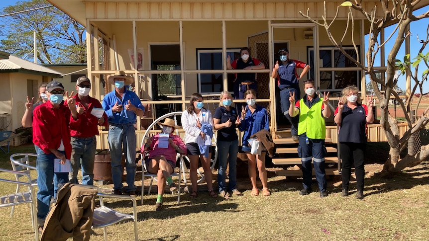 a group of station workers wearing masks standing in front of a small building.